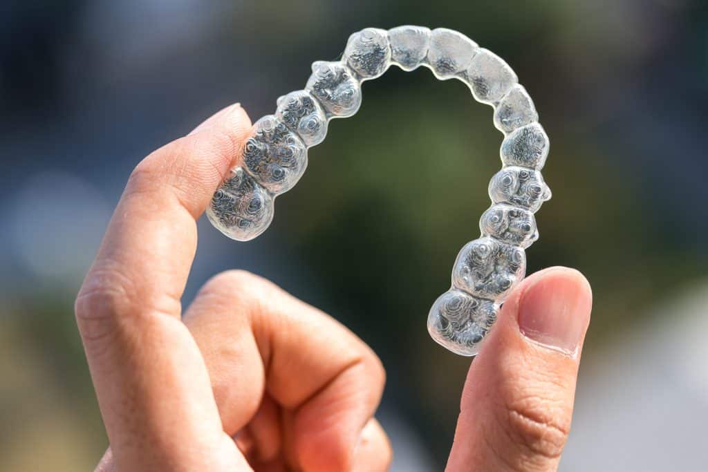 Chad Latino Blog Post Invisalign: Correct Your Smile With Clear Braces waco family dentist Holding invisalign braces on bokeh background