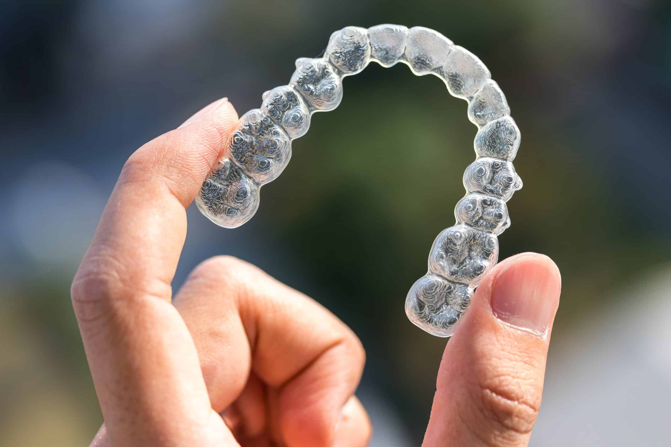 Chad Latino Blog Post Invisalign: Correct Your Smile With Clear Braces waco family dentist Holding invisalign braces on bokeh background